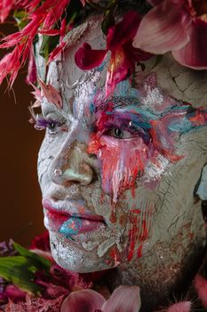 A girl smeared with clay. The model has a headdress made of flowers.