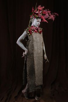 A girl smeared with clay. The model has a headdress made of flowers.