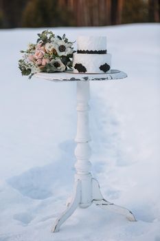 A cake in black and white design, standing on a stand in a winter forest on the snow.