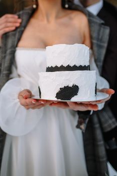 The bride and groom hold a wedding cake in their hands, standing in the snow in the forest.