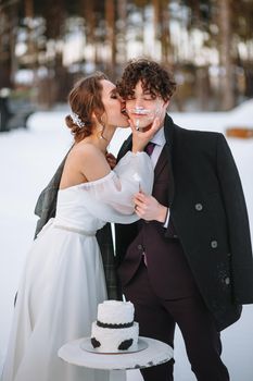 The bride licks the remains of the wedding cake from the groom. Shooting in the winter forest.