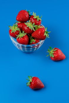 Bunch of strawberry in bowl on blue background. Yummy summer fruit