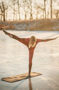 A girl does yoga in winter on the ice of the lake