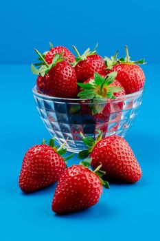 Bunch of strawberry in bowl on blue background. Yummy summer fruit