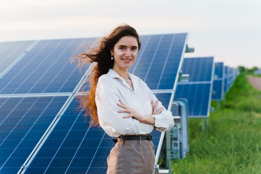 Model with solar panels stands in row on the ground. Girl dressed white formal shirt smiles on the power plant