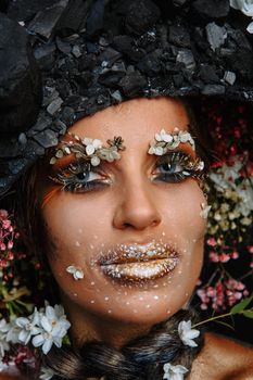 A large portrait of a model in a headdress made of coal. Bright makeup and body.