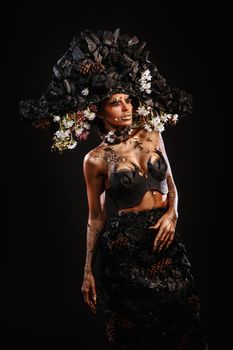 Portrait of a model in a headdress and dress made of coal. Bright makeup and body art.