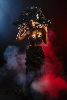 Portrait of a model in a headdress and dress made of coal. There is red smoke behind the model.