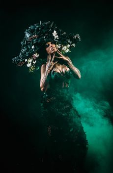 Portrait of a model in a headdress and dress made of coal. There is green smoke behind the model.