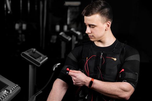 Handsome trainer in EMS suit with red wires for electro impulse stimulation for body. Training in gym