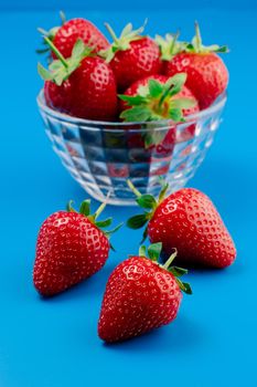 Bunch of strawberry in bowl on blue background. Yummy summer fruit