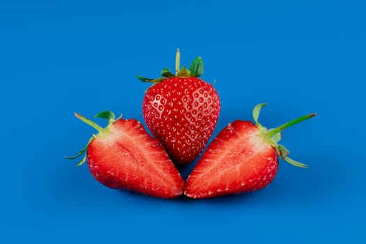 Strawberry slices close-up and full piece of strawberries on blue background. Seasonal berry.
