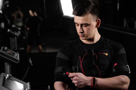 Handsome trainer in EMS suit with red wires for electro impulse stimulation for body. Training in gym