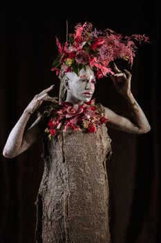 A girl smeared with clay. The model has a headdress made of flowers.