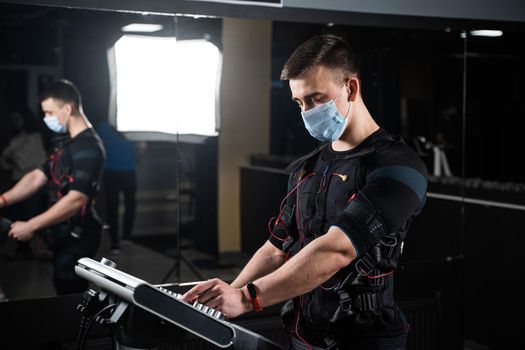 Man in EMS suit and medical mask in gym. Protection from coronavirus covid-19. Sport training in electrical muscle stimulation suit at quarantine period