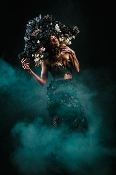 Portrait of a model in a headdress and dress made of coal. There is green smoke behind the model.