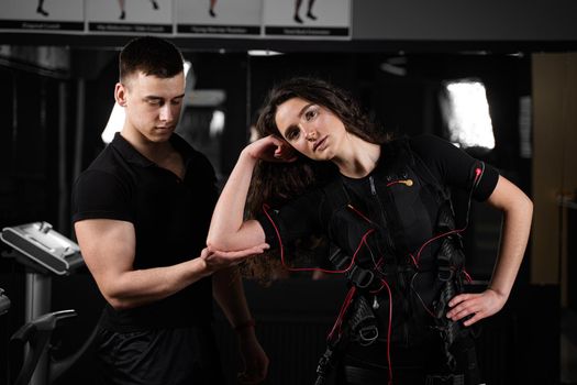 Man trainer trains a girl in an EMS suit in the gym. Electrical stimulation of the misc during active training.