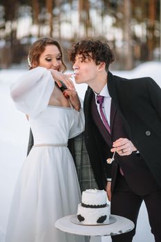 The groom licks the remains of the wedding cake from the bride's finger. Shooting in the winter forest.