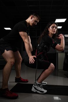 Man trainer trains a girl in an EMS suit in the gym. Electrical stimulation of the misc during active training.