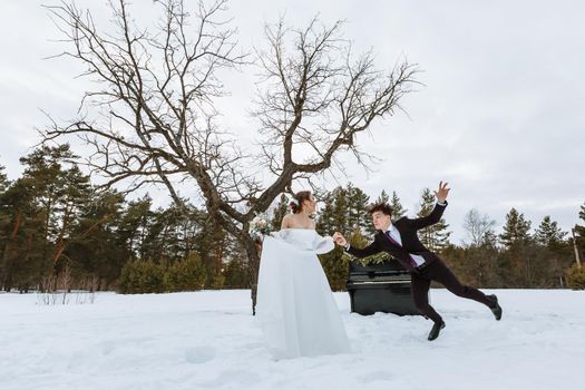 The bride holds the groom's hand. Winter forest, with a piano in the background.