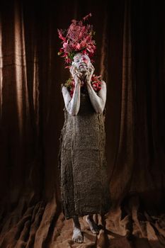 A girl smeared with clay. The model has a headdress made of flowers.