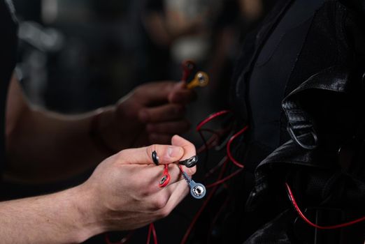 Wires from EMS suit in gym. Sport training in electrical muscle stimulation suit. Making physical exercises.