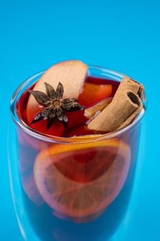 Mulled wine on blue background. Alcohol punch in double glass cup. Drink with orange, anise star, cinnamon and apple