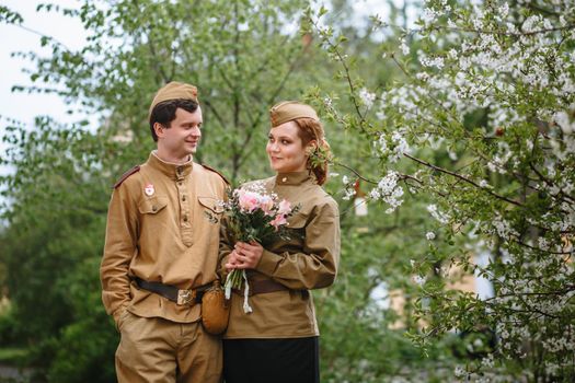 Portrait of two military lovers at a flowering tree. Warm spring, people are returning from the war