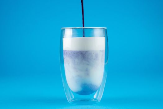Pouring purple goji matcha in double glass cup. Matcha cocktail on blue background