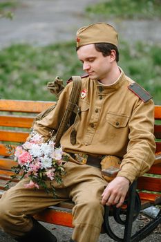 A soldier sitting on a bench waiting with a bouquet in his hands