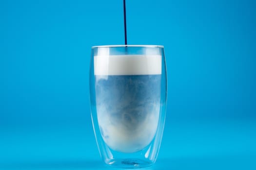 Pouring blue anchan matcha latte in double glass cup. Matcha cocktail on blue background