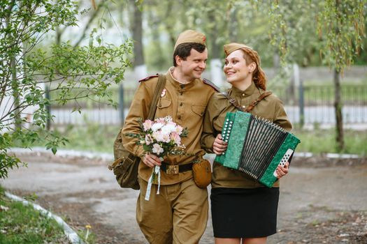 A soldier walks down the alley, hugging a military girl playing an accordion, spring, people returned from the war