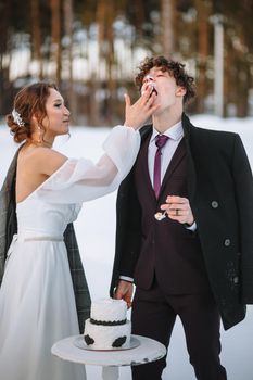 The bride wants to smear the groom's face with a piece of wedding cake. Shooting in the winter forest.