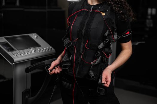 Girl in EMS suit in gym. Sport training in electrical muscle stimulation suit. Making physical exercises.