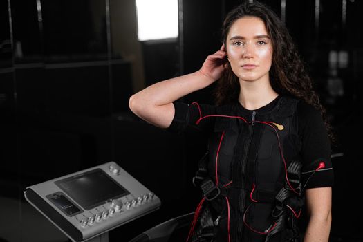 Girl in EMS suit in gym. Sport training in electrical muscle stimulation suit. Making physical exercises.