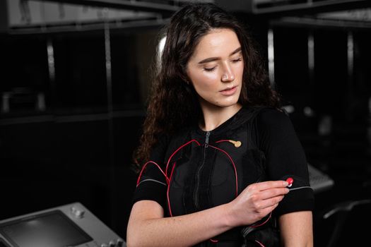 Girl in EMS suit in gym. Sport training in electrical muscle stimulation suit. Making physical exercises.