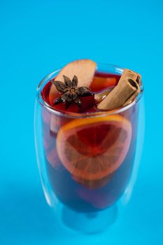 Mulled wine on blue background. Alcohol punch in double glass cup. Drink with orange, anise star, cinnamon and apple