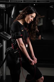 Girl in EMS suit in gym. Sport training in electrical muscle stimulation suit. Making physical exercises.