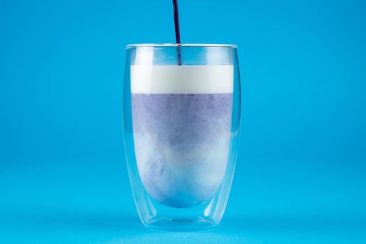 Pouring purple goji matcha in double glass cup. Matcha cocktail on blue background