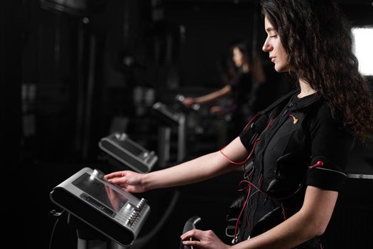 Girl in EMS suit in gym. Sport training in electrical muscle stimulation suit