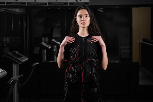 Girl in EMS suit in gym. Sport training in electrical muscle stimulation suit