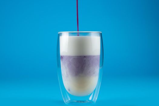 Pouring purple goji matcha in double glass cup. Matcha cocktail on blue background