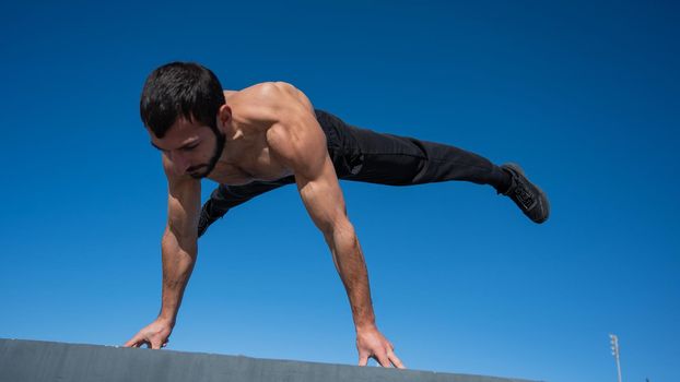 Shirtless man doing a handstand on a parapet by the sea