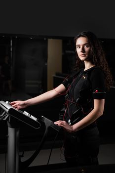 Girl in EMS suit in gym. Sport training in electrical muscle stimulation suit