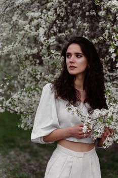 Lovely girl near blooming trees in the park. Outdoor walking in at sunny day. Lifestyle of young woman