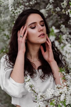 Portrait of young woman in the garden. Attractive girl weared white dress posing near blooming trees