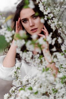 Portrait of young woman in the garden. Attractive girl weared white dress posing near blooming trees