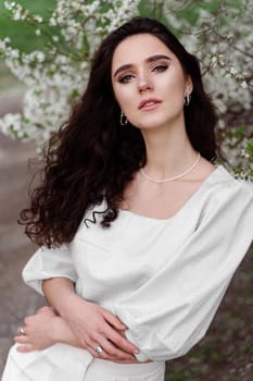 Spring lifestyle. Model posing near white blooming trees without mask outdoor countryside. Dreaming girl with curly hair