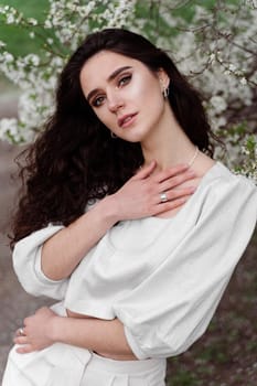 Spring lifestyle. Model posing near white blooming trees without mask outdoor countryside. Dreaming girl with curly hair