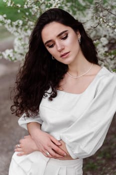 Spring lifestyle. Model posing near white blooming trees without mask outdoor countryside. Dreaming girl with curly hair